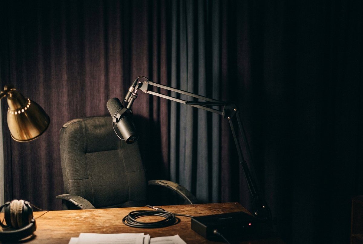 Een microfoon aan een scharnierende arm die dicht bij een lege bureaustoel is gedraaid, met zware gordijnen erachter
